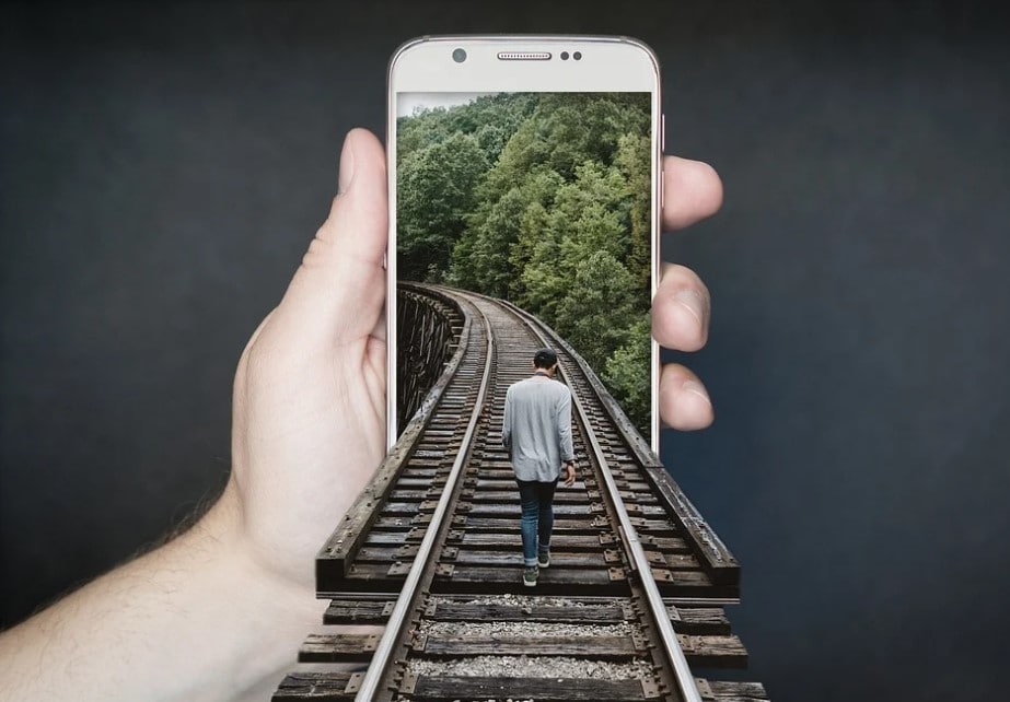 Celular com imagem de trilhos de trem, onde uma pessoa caminha por cima dele. Alinhe a campanha de publicidade